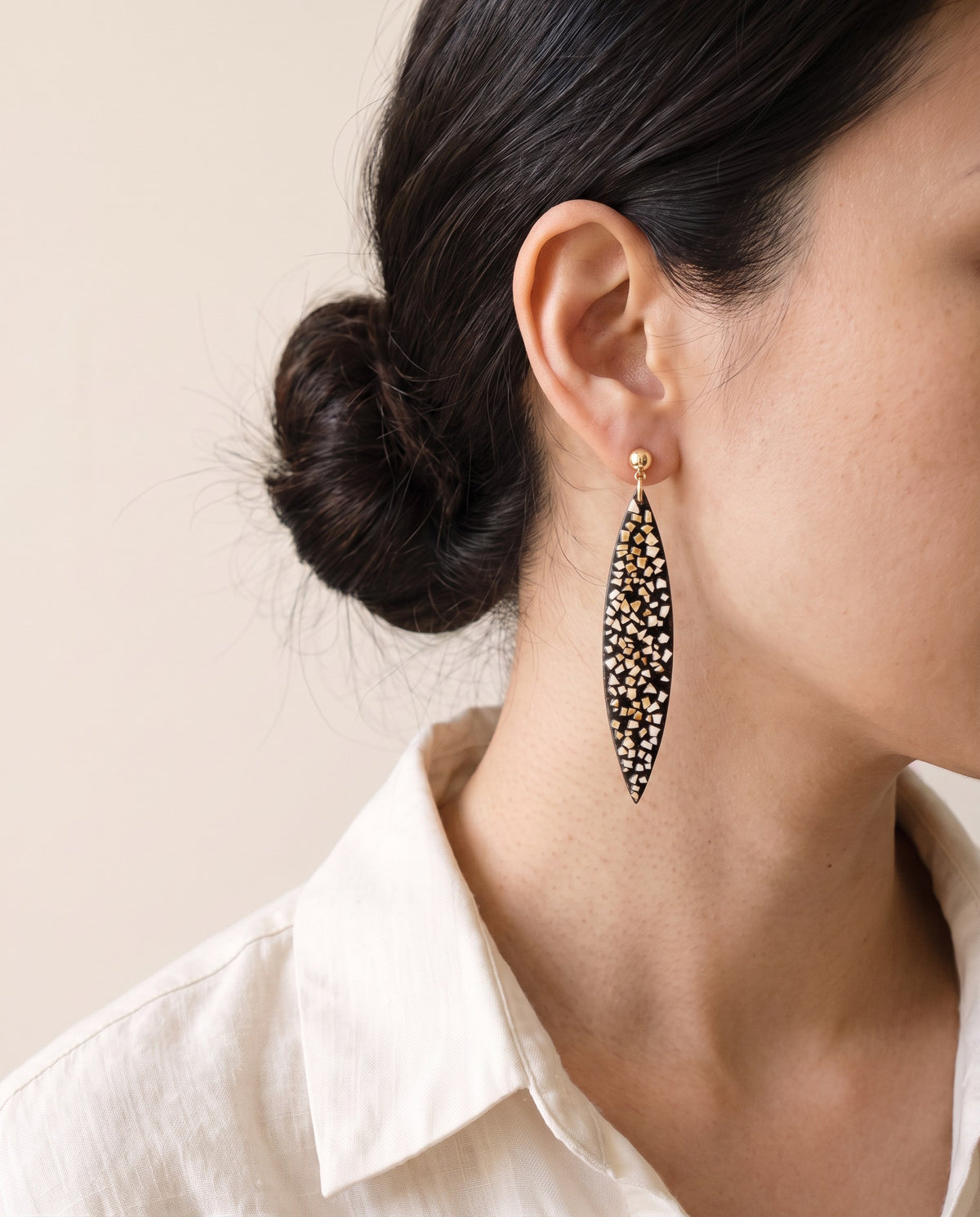 Long black lacquer leaf earring inlaid with white and honey eggshell on a gold ball stud, worn with a linen shirt