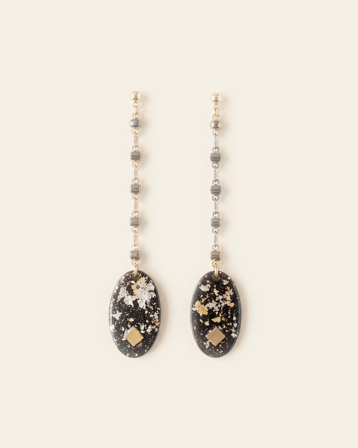 Pair of long chain drop earrings with flat black oval lacquer pendants flecked with gold and silver leaf, on gold ball studs against an ivory background