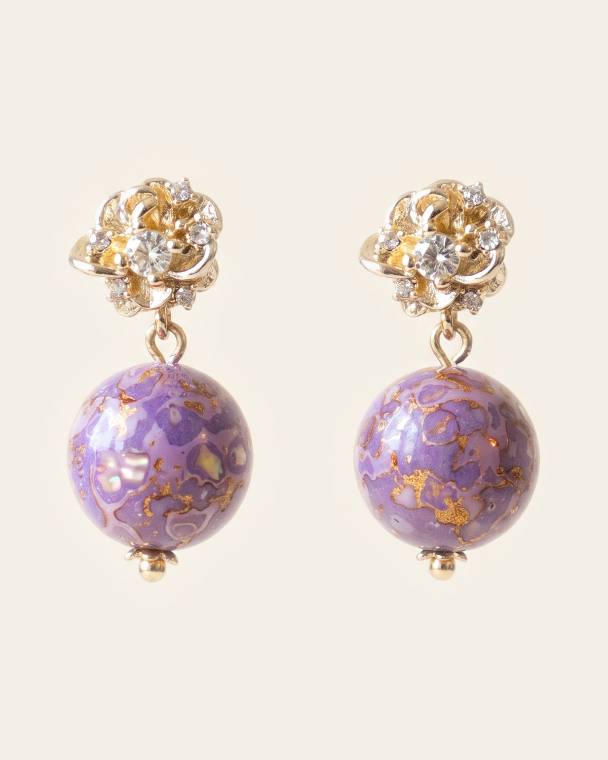 Pair of drop earrings with gold flower studs set with clear stones and lilac marbled lacquer spheres inlaid with mother-of-pearl, on an ivory background