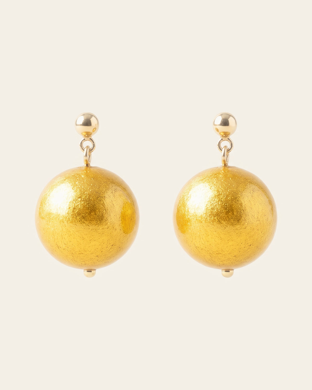 Pair of small drop earrings: gold ball studs and round lacquer beads laid with bright golden-yellow gold leaf, on an ivory background