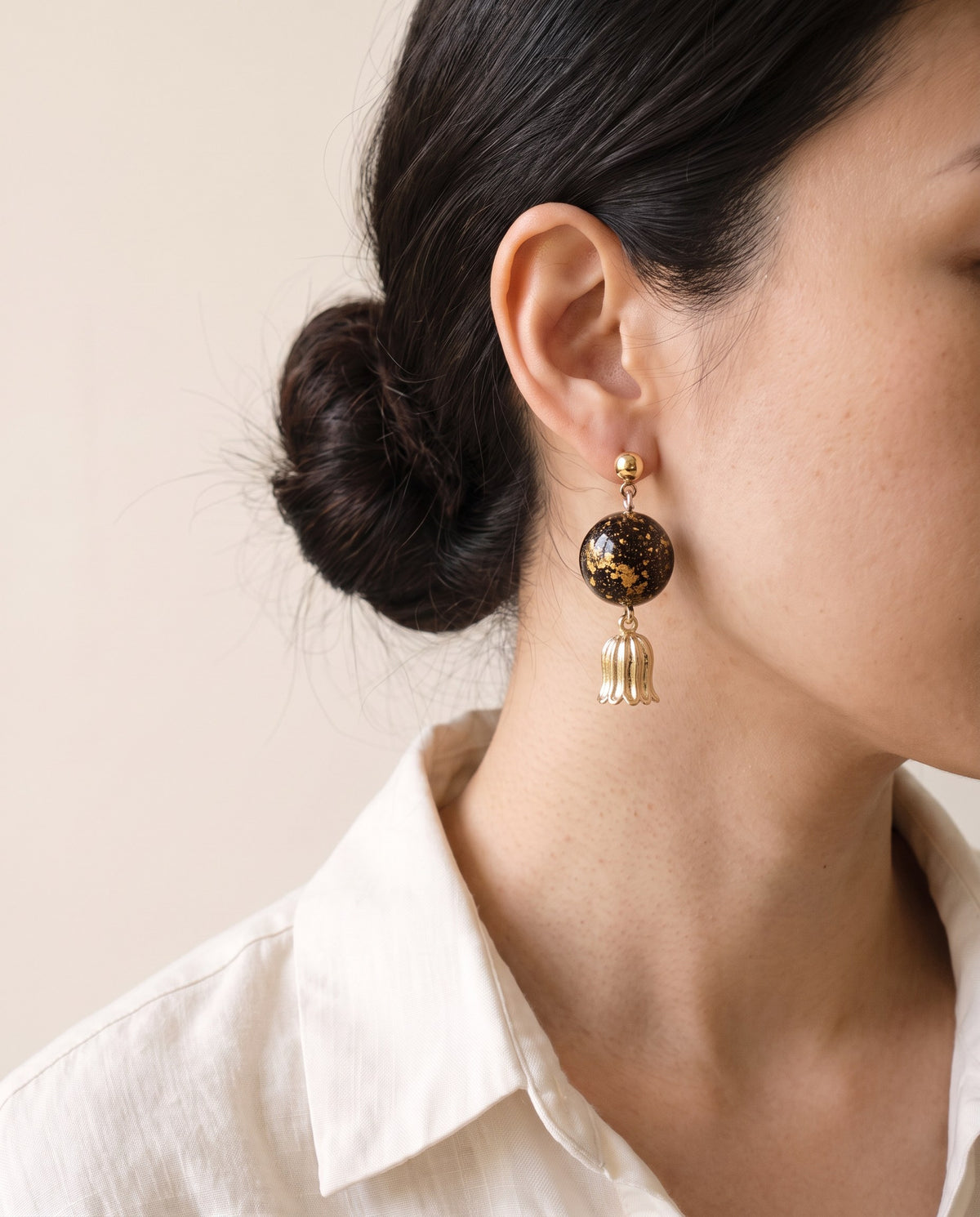Black lacquer bead scattered with gold leaf on a gold ball stud, with a fluted gold bellflower drop, worn with a linen shirt