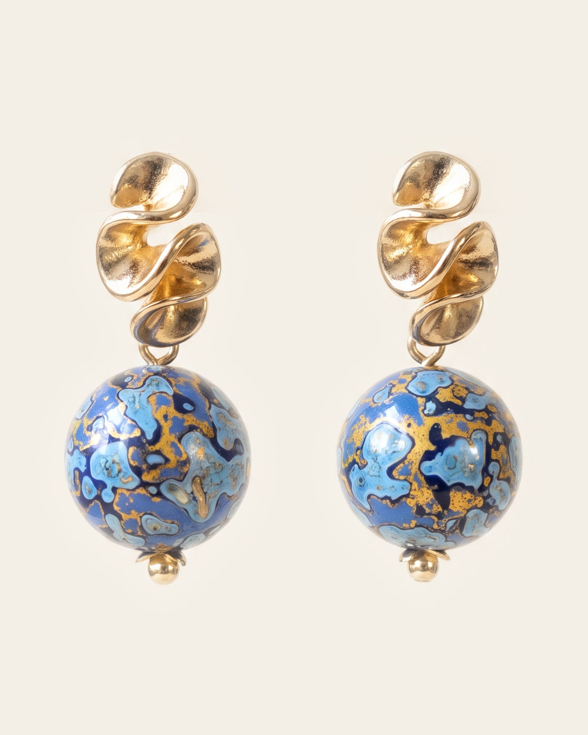 Pair of stud drop earrings with ruffled gold studs above round deep blue xipi lacquer beads marbled with pale blue and gold, on an ivory background