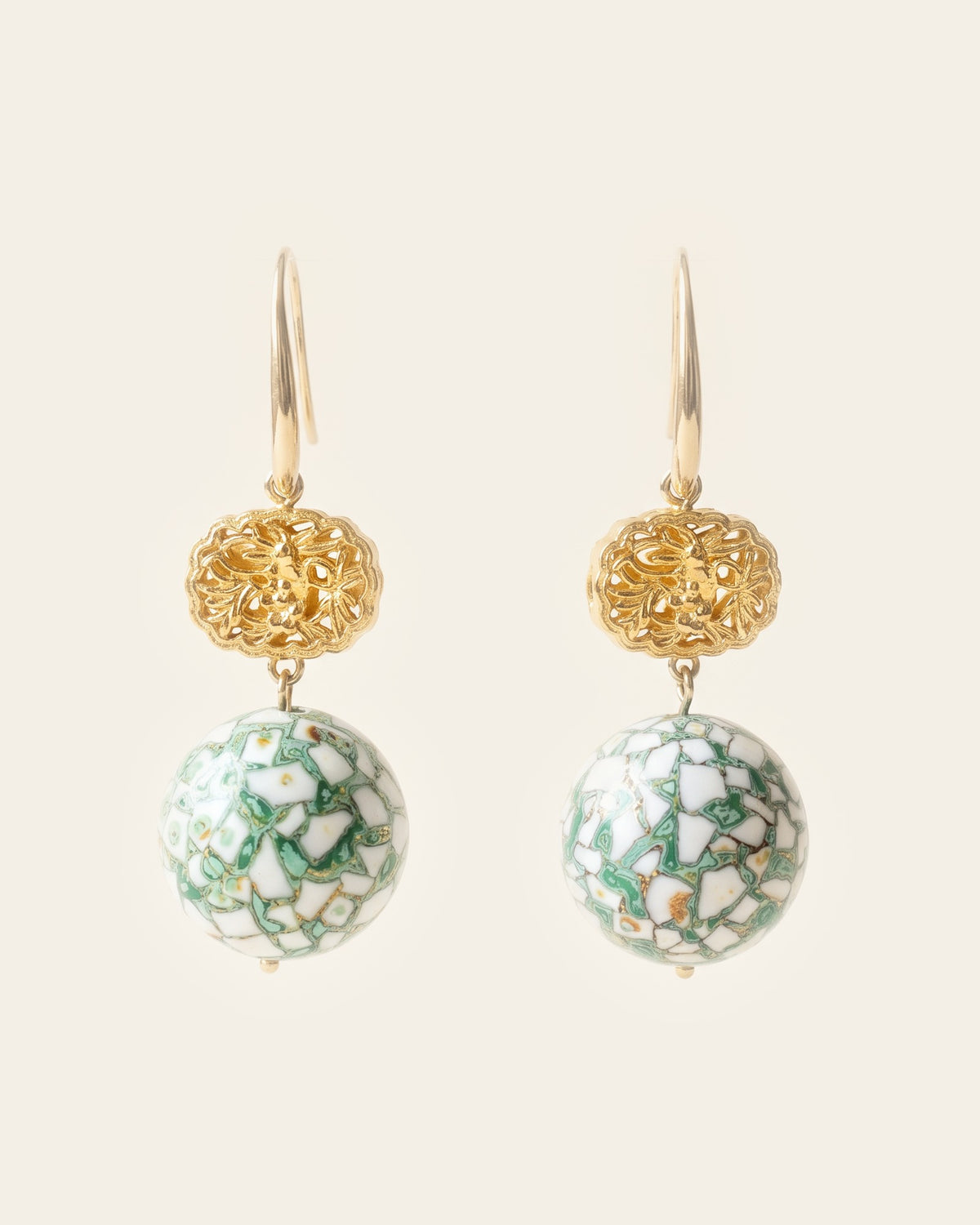 Pair of drop earrings: 14k gold hooks, oval openwork 18k gold flower beads, and round beads of white duck eggshell inlay set in green lacquer, on a cream background.