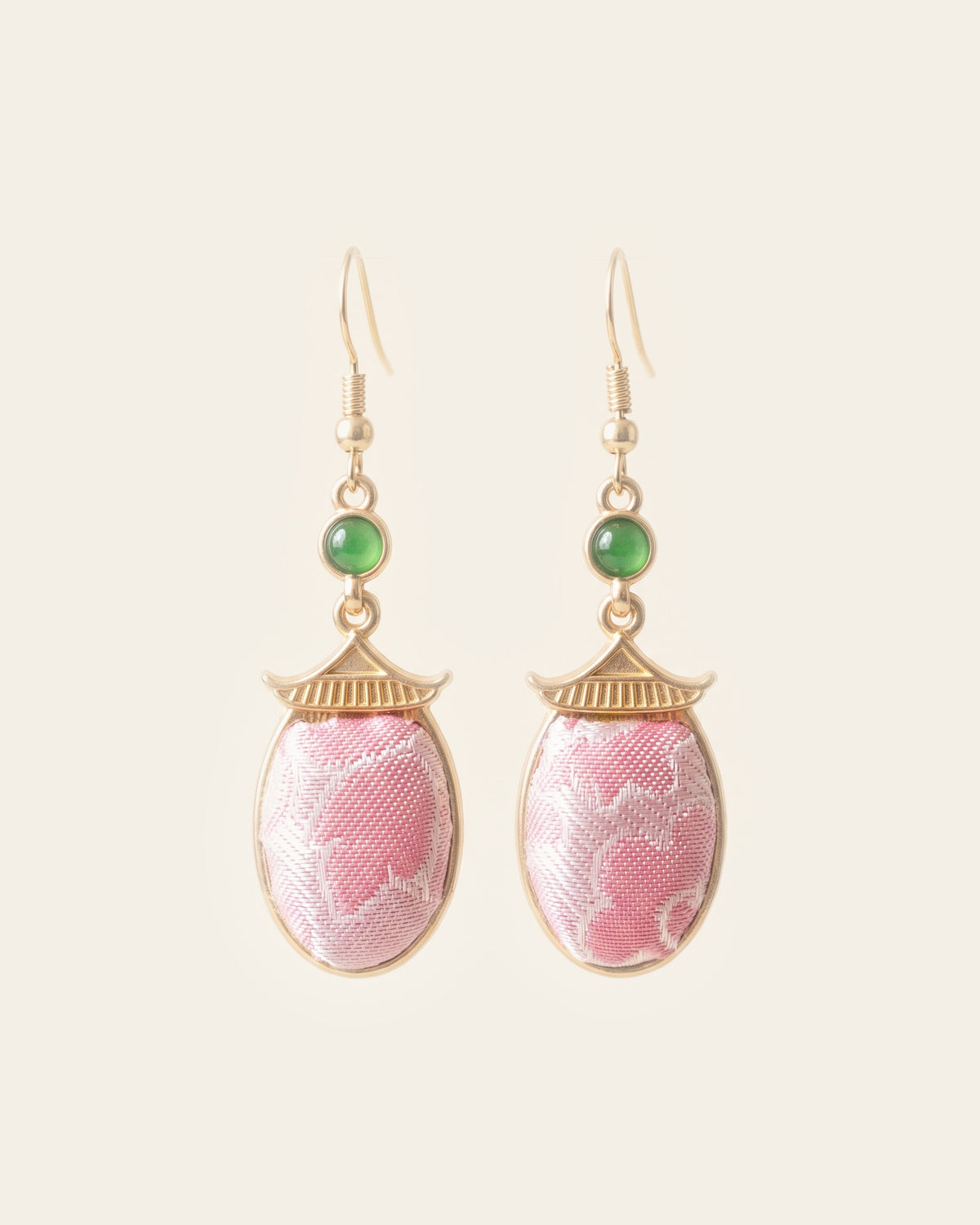 Pair of drop earrings with oval pink Song brocade panels under gold-tone pagoda-roof caps and small green cabochons, hanging from gold-tone hooks on an ivory background