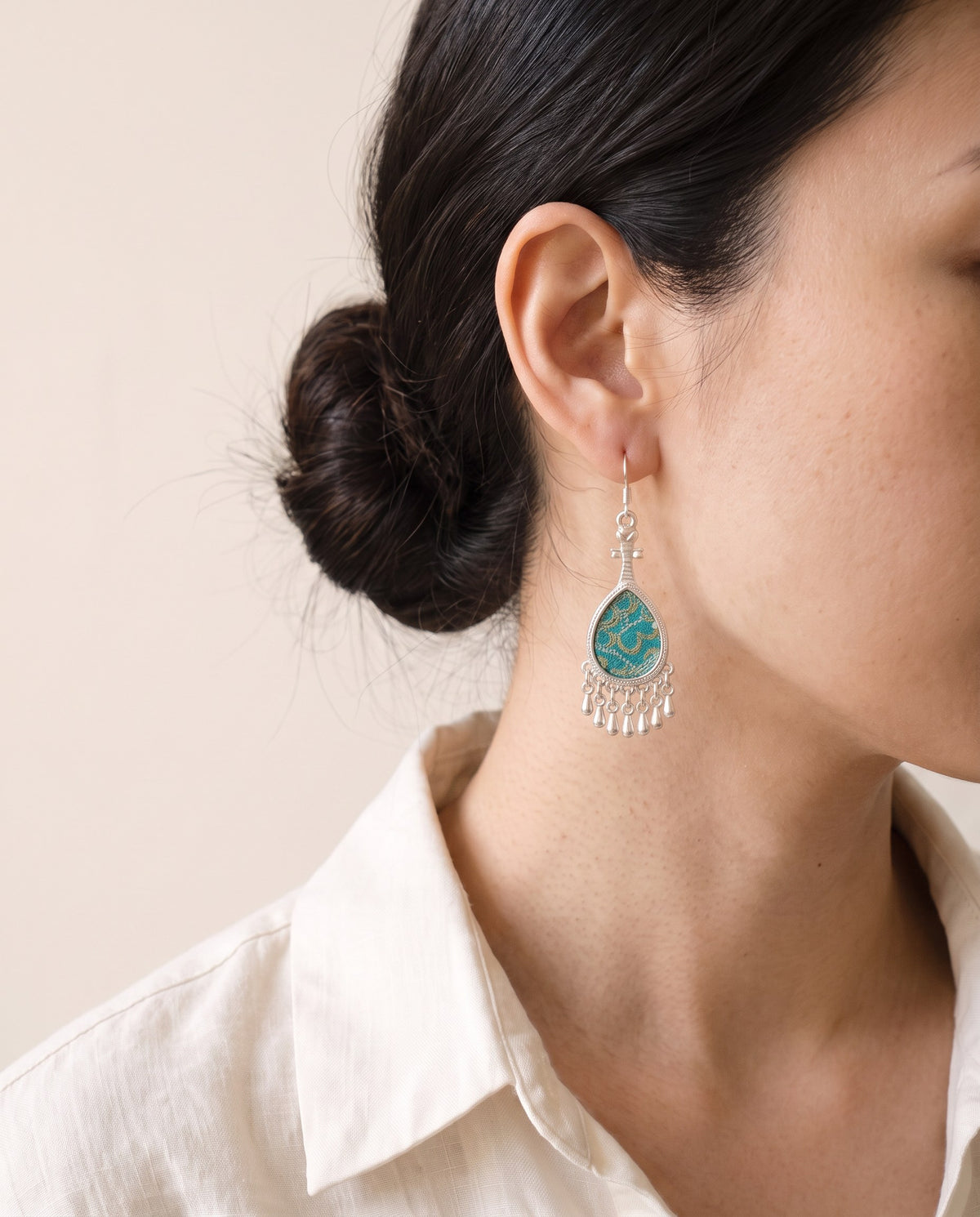 Turquoise Song brocade pipa earring in Miao silver with a silver teardrop fringe, worn with a linen shirt