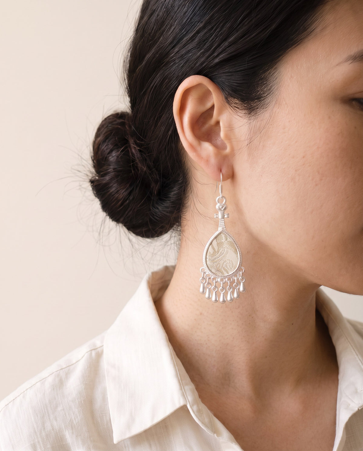Ivory Song brocade pipa earring in matte silver with a teardrop fringe, worn with a linen shirt