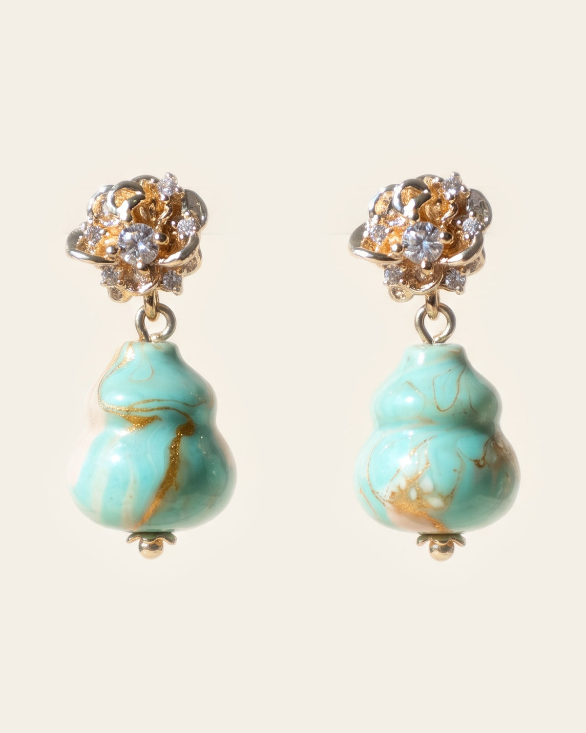 Pair of stud drop earrings with gold rose studs set with clear stones above mint-green double-gourd lacquer beads swirled with peach and gold, on an ivory background