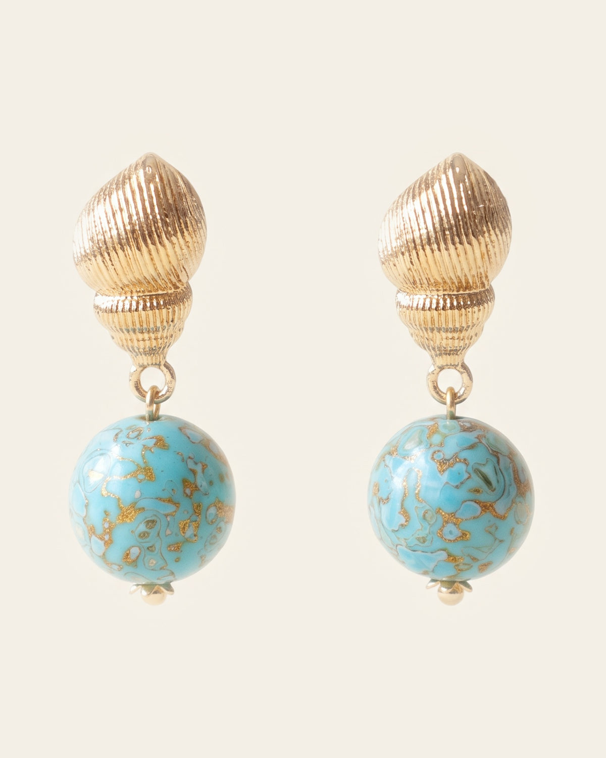Pair of drop earrings: ribbed gold seashell post studs holding round turquoise xipi lacquer beads marbled with brown and gold, on an ivory background.