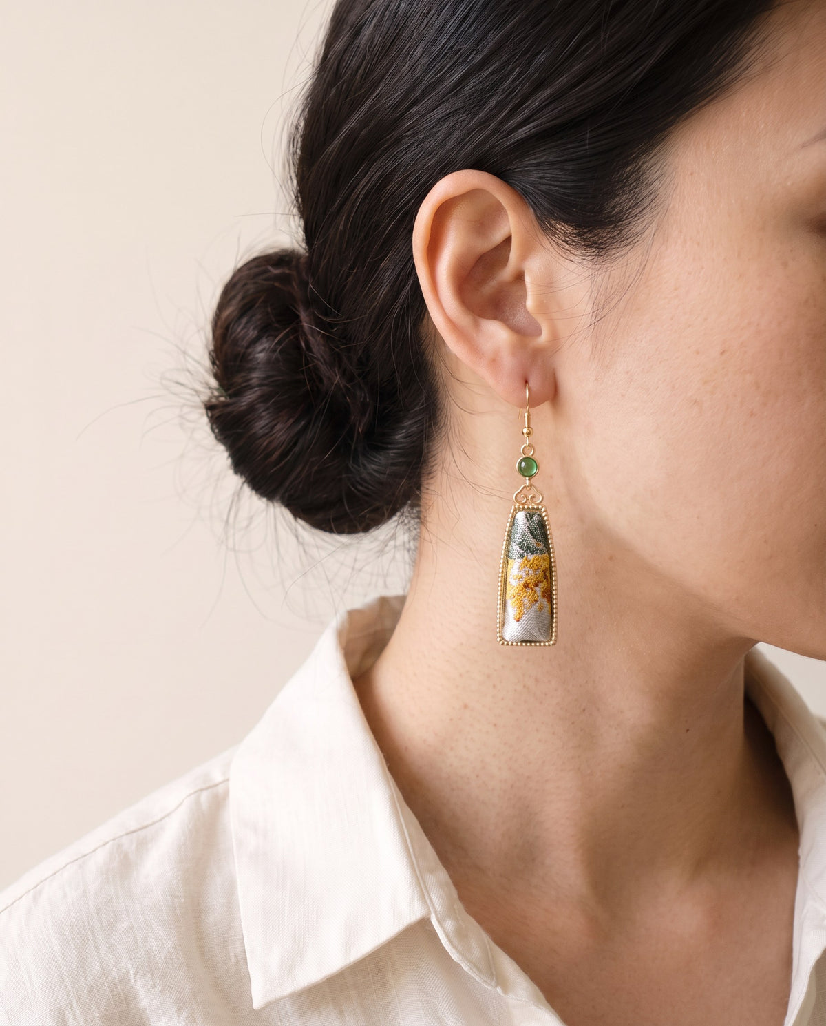 Green and gold floral Song brocade tapered earring with a green stone and gold-tone hook, worn with a linen shirt
