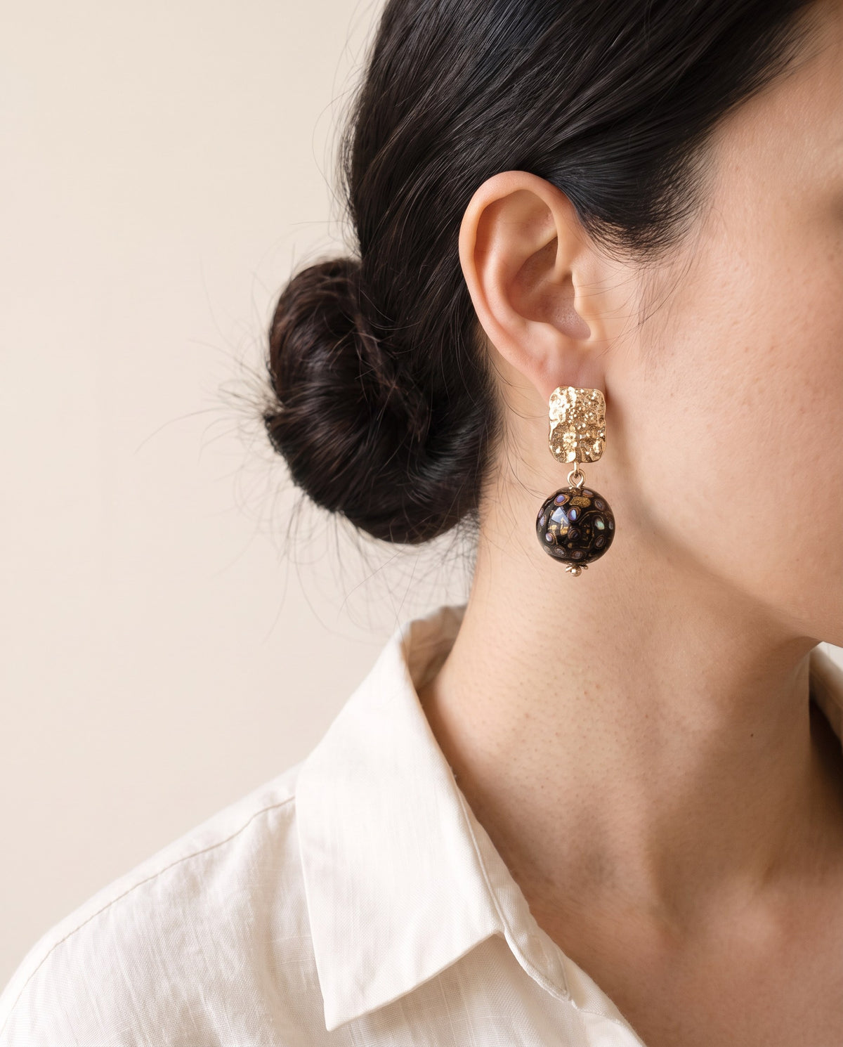 Black Xipi lacquer bead with mother-of-pearl flecks hanging from a hammered gold stud, worn with a linen shirt