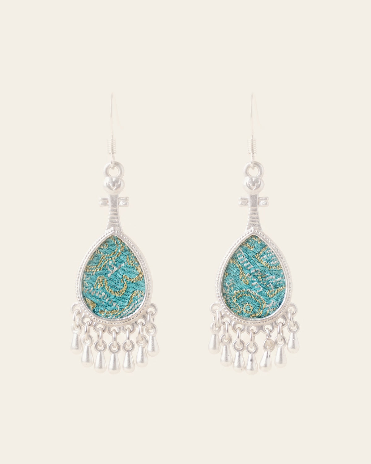 Pair of silver-tone pipa-shaped drop earrings set with turquoise Song brocade and finished with a fringe of small silver teardrops, on silver-tone hooks against an ivory background