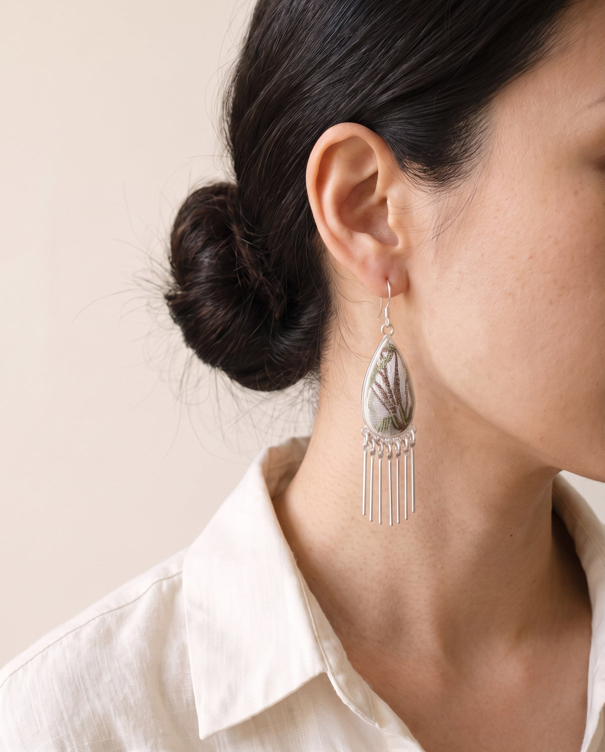 Silver-blue Song brocade teardrop earring on a silver hook with a seven-bar silver fringe, worn with a linen shirt