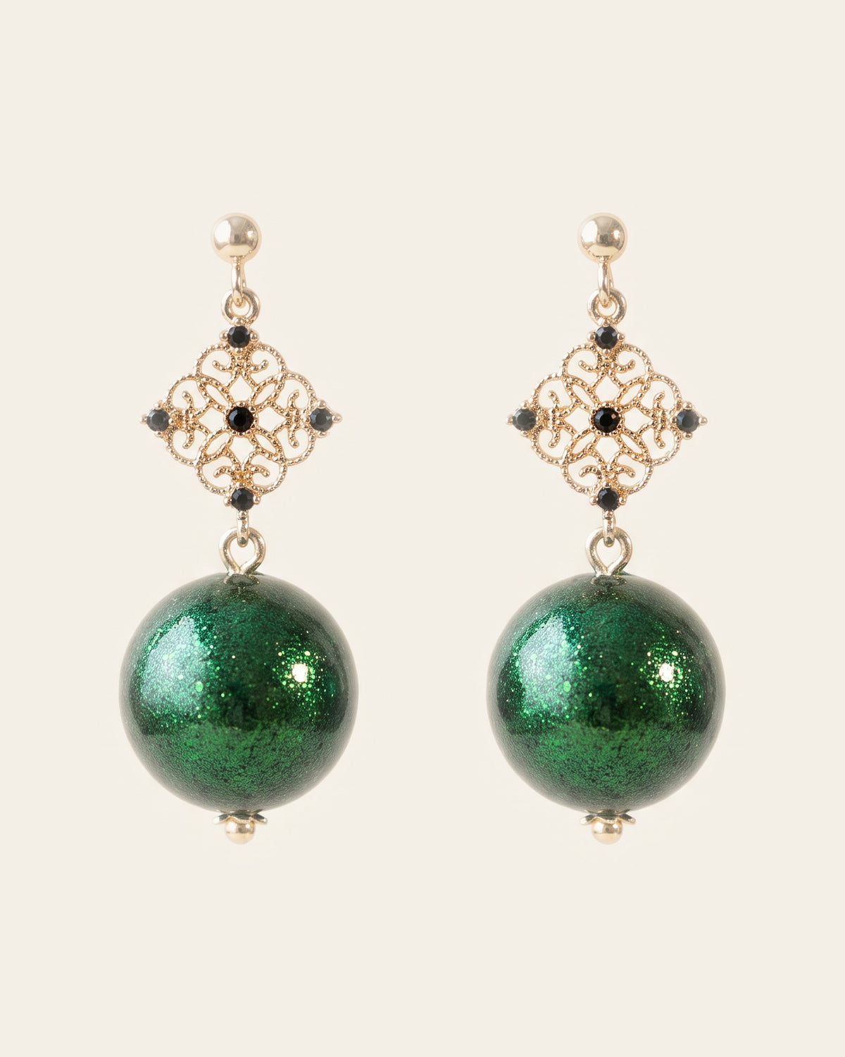 Pair of drop earrings with gold ball studs, gold filigree diamonds set with black stones and emerald-green shimmering lacquer spheres, on an ivory background