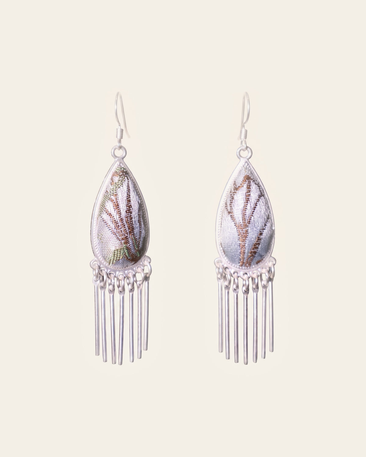 Pair of drop earrings: teardrops of pale silver-blue Song brocade with brown leaf pattern in Miao silver frames, each with a fringe of seven silver bars, on silver-tone hook ear wires, on an ivory background.