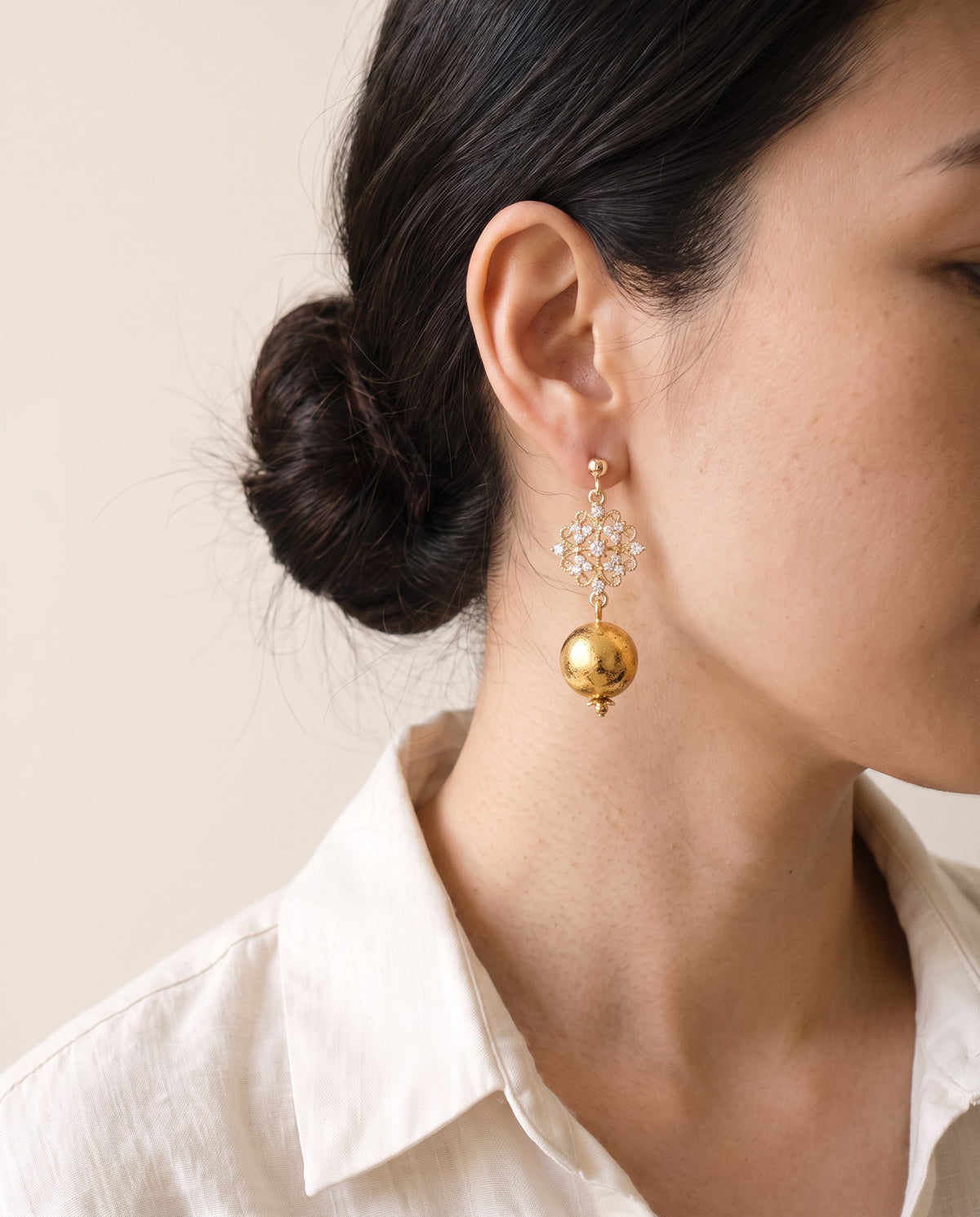 Gold leaf lacquer sphere below a gold filigree diamond set with clear stones on a ball stud, worn with a linen shirt
