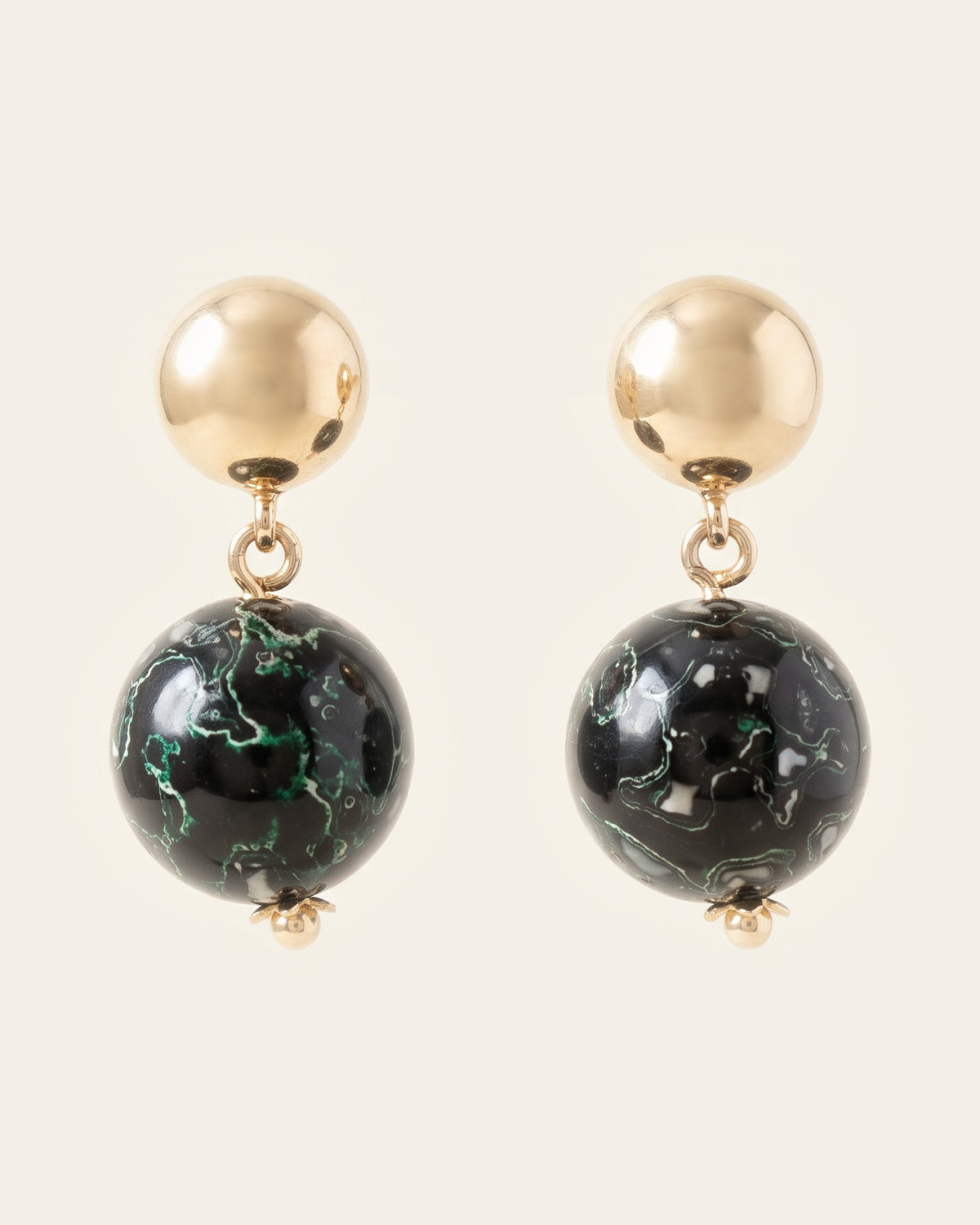 Pair of black and green marbled lacquer sphere earrings hanging from large gold ball studs on an ivory background