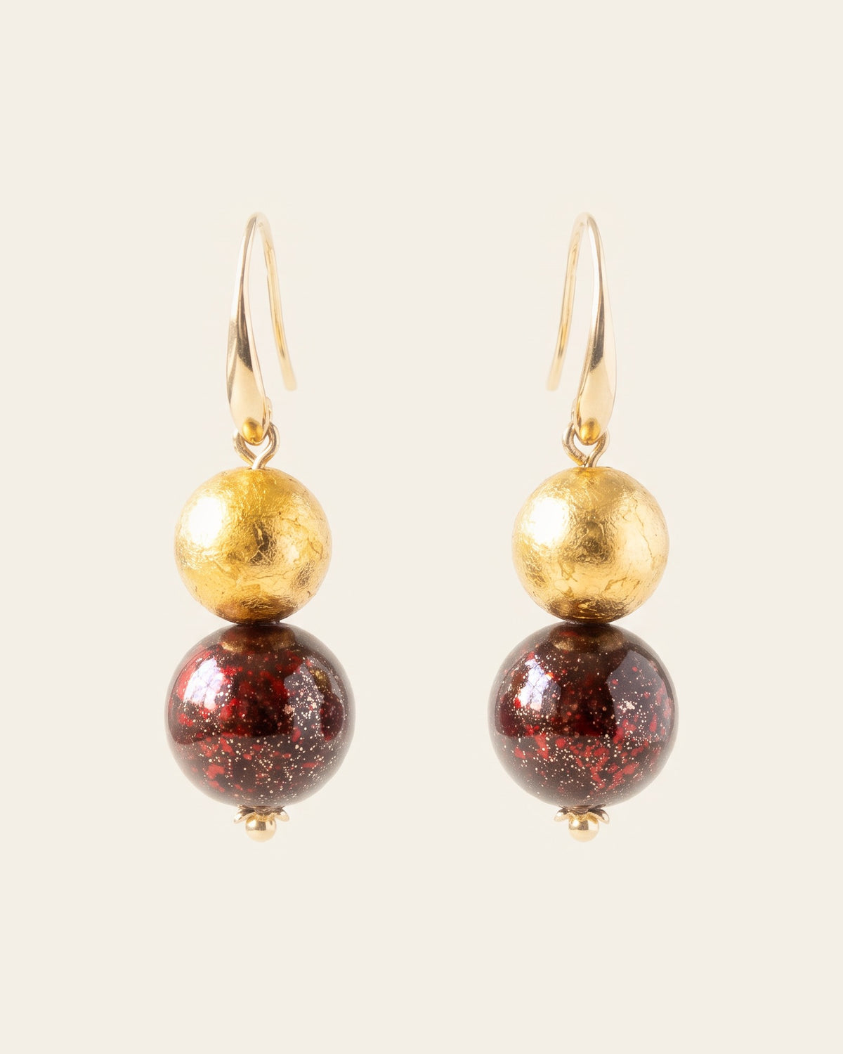 Pair of drop earrings with gold hooks, a gold-leaf bead above a larger red-flecked lacquer bead, on an ivory background