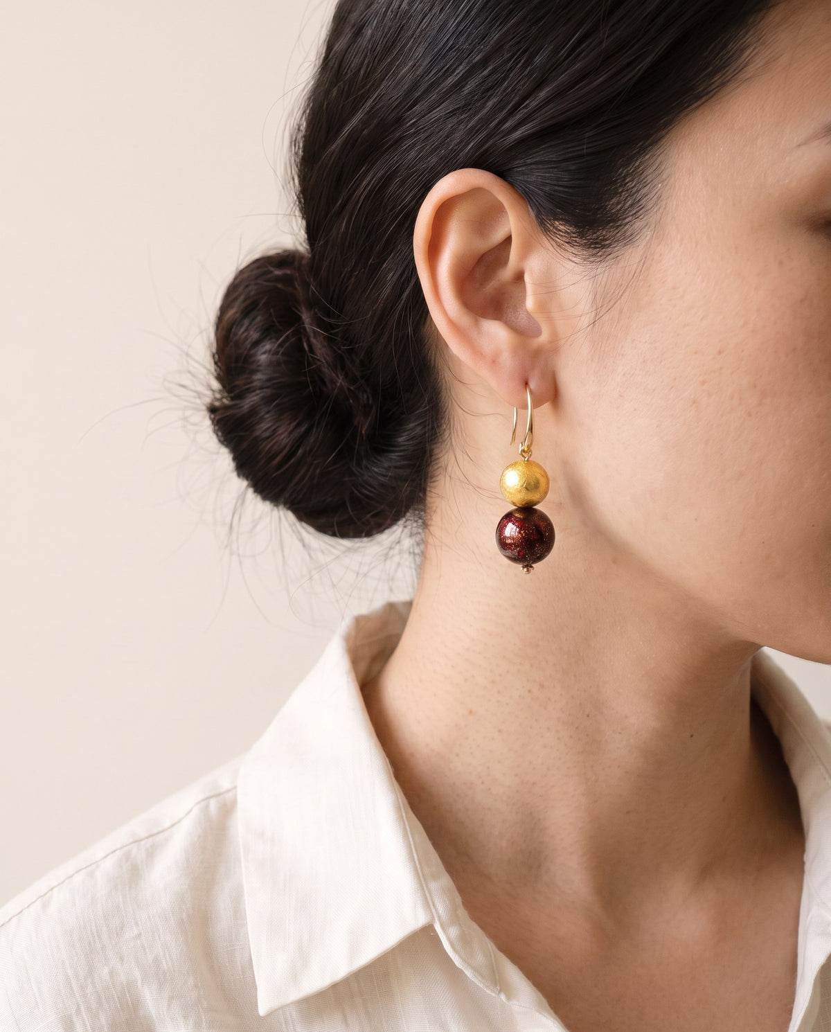 Gold leaf lacquer bead above a deep red flecked lacquer bead on a gold ear hook, worn with a linen shirt