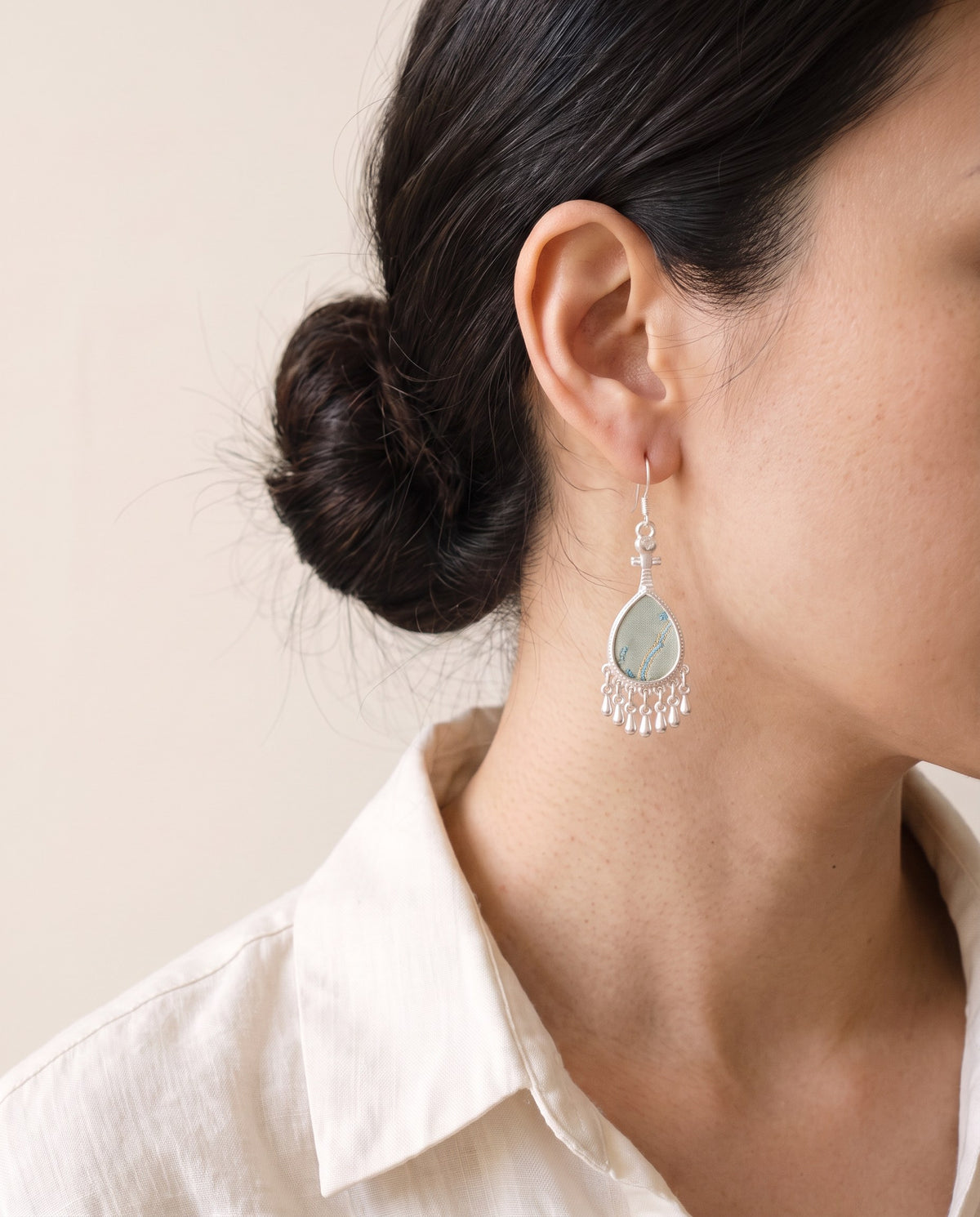 Sage Song brocade pipa earring with a blue river motif and a silver teardrop fringe, worn with a linen shirt