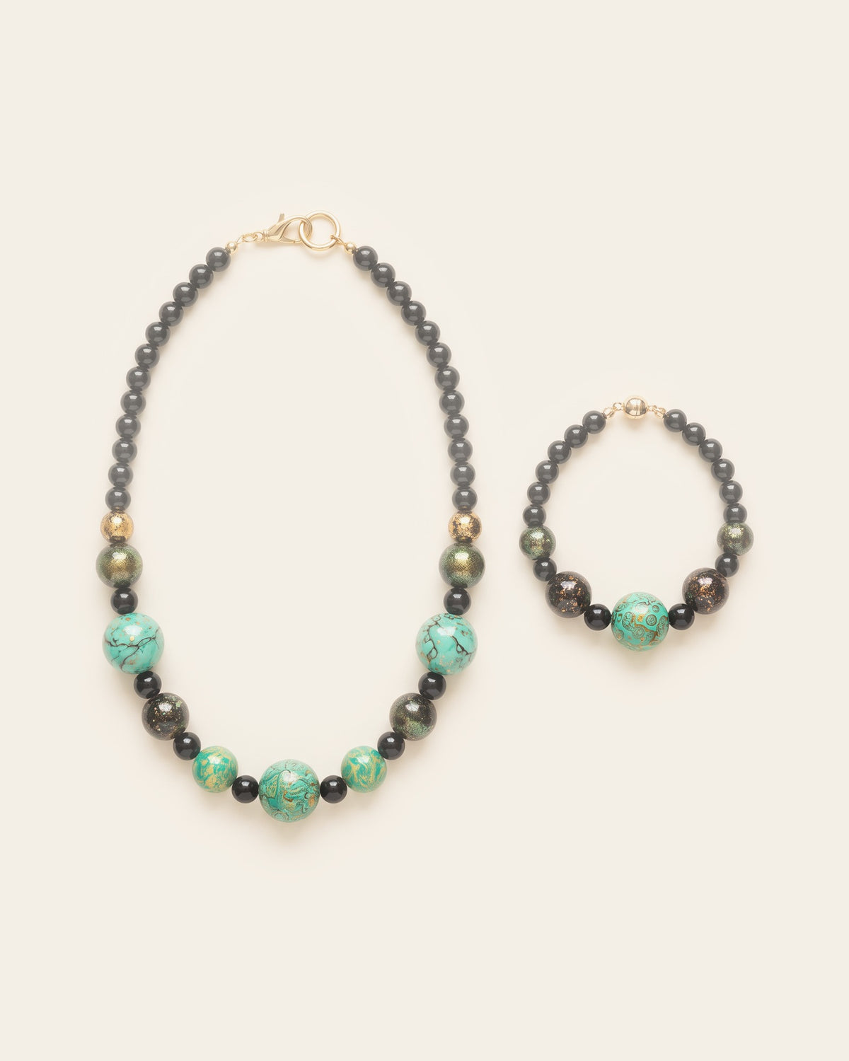 Bead necklace and bracelet set in black, gold-fleck and green xipi lacquer beads with a turquoise mother-of-pearl bead, laid flat on an ivory background