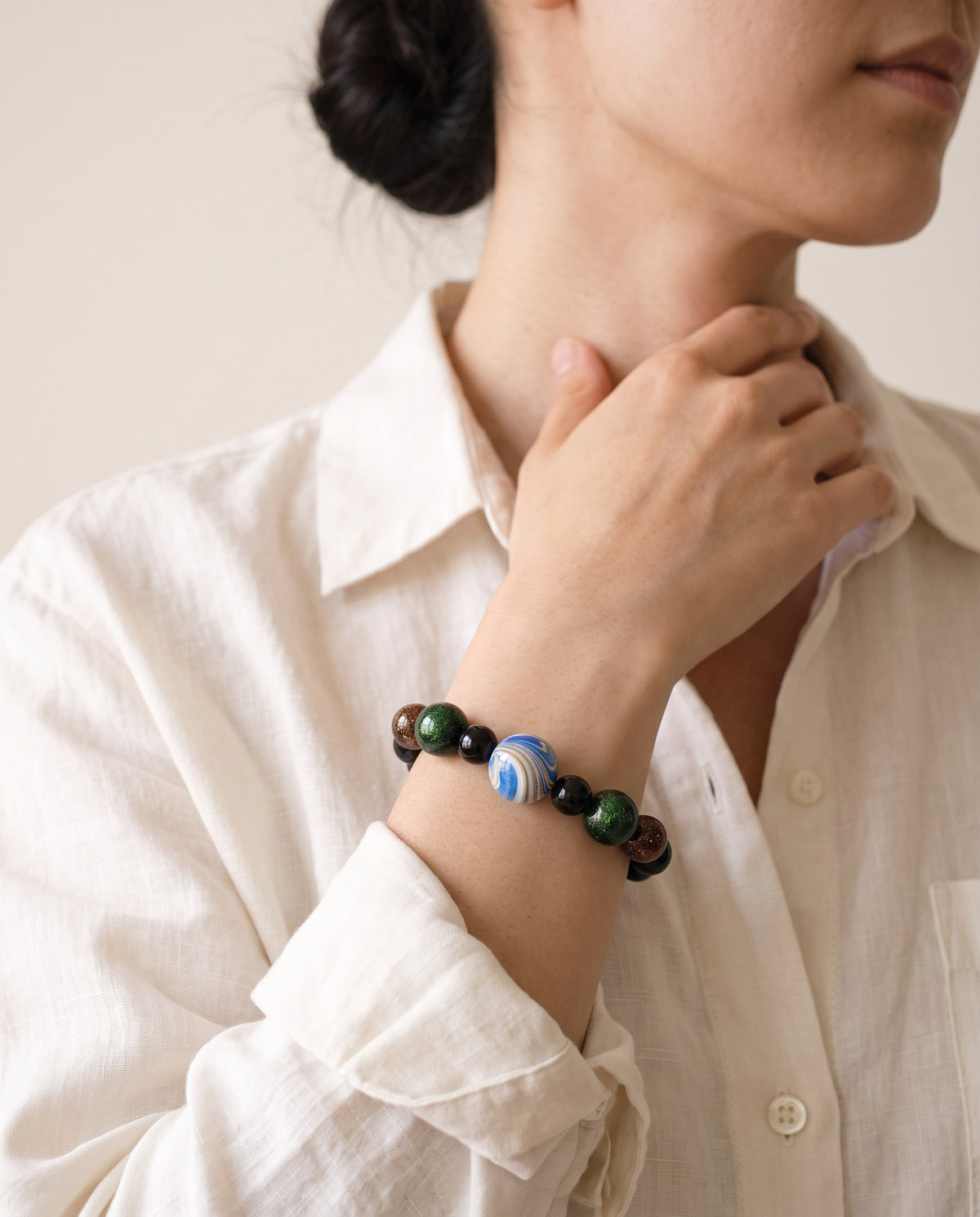 Black lacquer bead bracelet with a blue marbled xipi centre bead, worn on the wrist with a linen shirt
