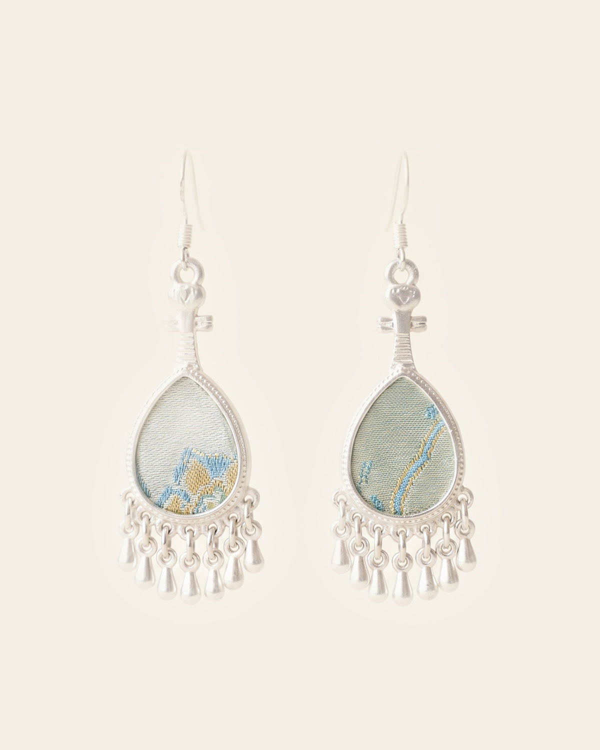 Pair of pipa-shaped silver earrings with teardrop sage-green brocade panels and a fringe of seven silver drops, on an ivory background