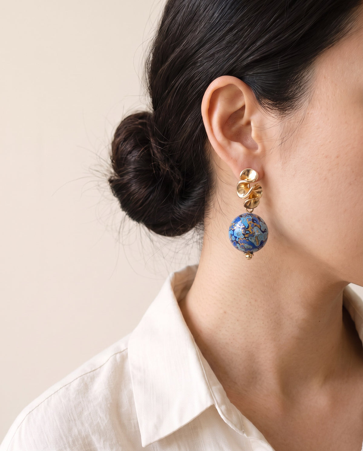 Blue marbled Xipi lacquer bead earring below a gold ruffle stud, worn with a linen shirt