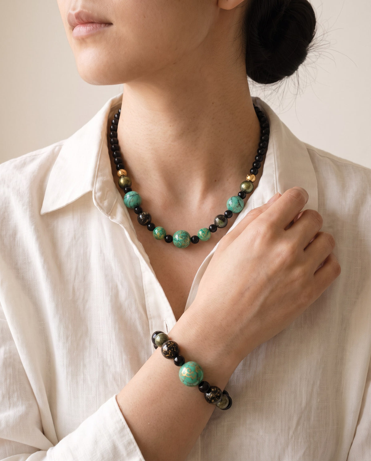 Green xipi lacquer bead necklace with black and gold-leaf beads at the collarbone, and the matching bracelet on her wrist, worn with a linen shirt