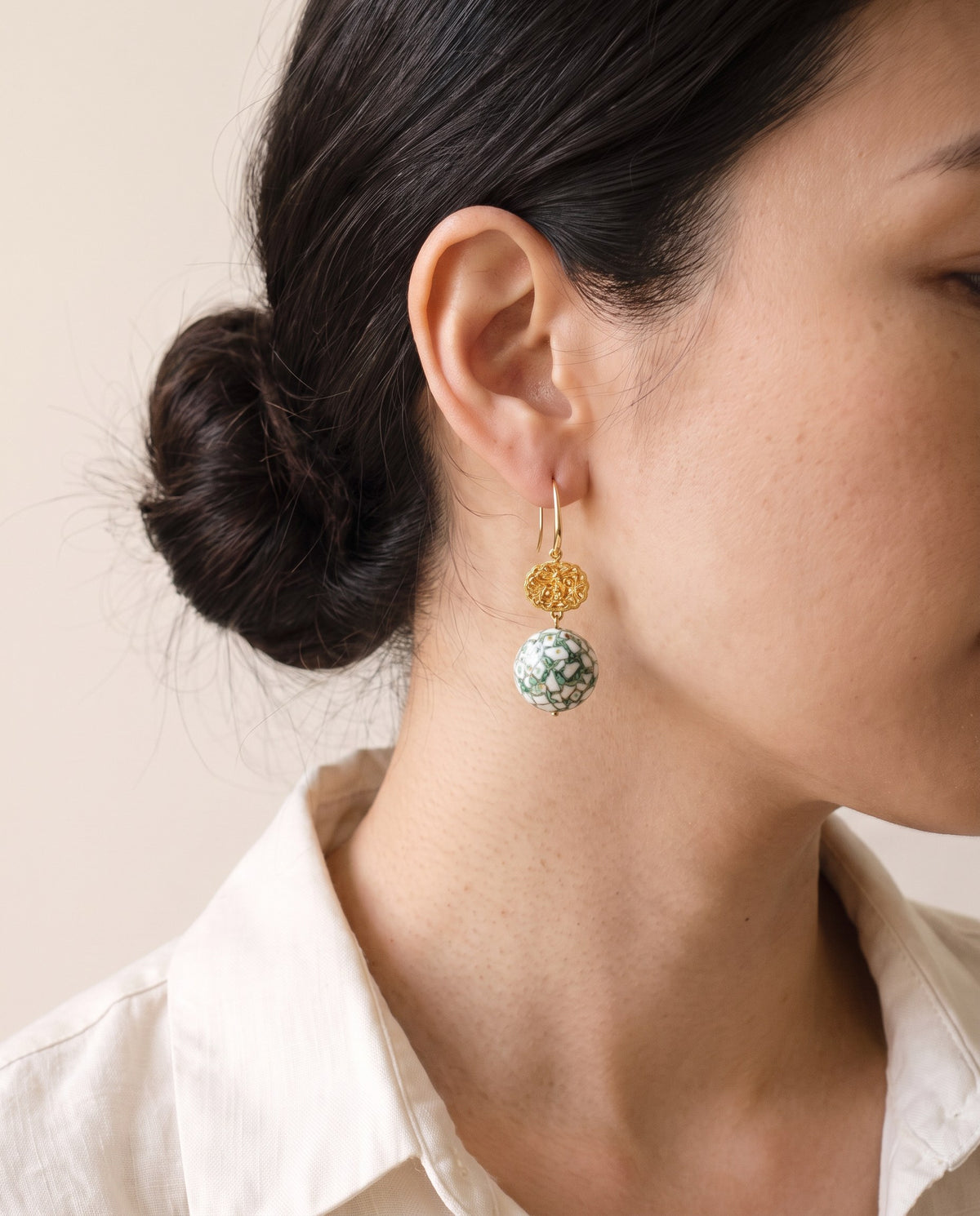 Green and white eggshell lacquer sphere below a gold openwork filigree bead on a gold hook, worn with a linen shirt