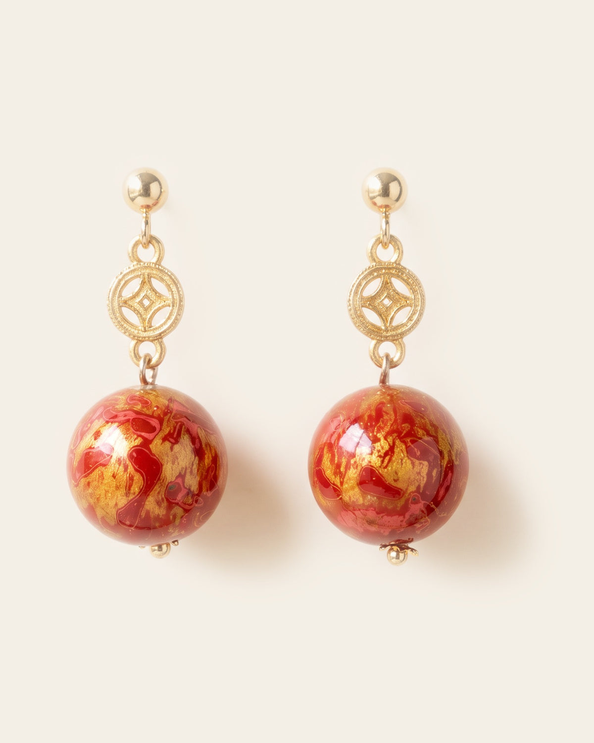 Pair of red and gold marbled lacquer sphere earrings with openwork gold coin charms on gold ball studs, on an ivory background