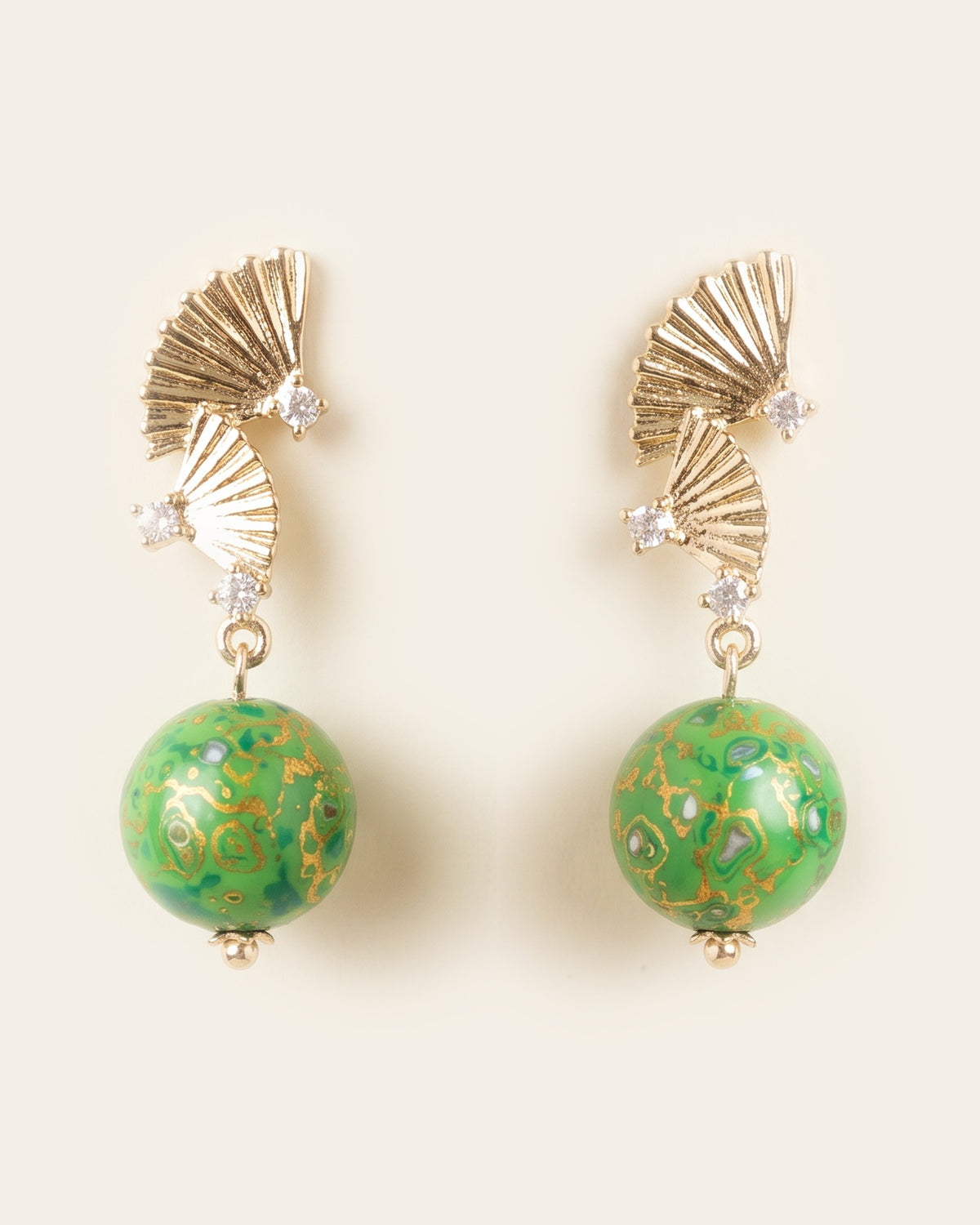 Pair of stud drop earrings with two pleated gold fans set with clear stones above round green xipi lacquer beads marbled with gold and mother-of-pearl flecks, on an ivory background