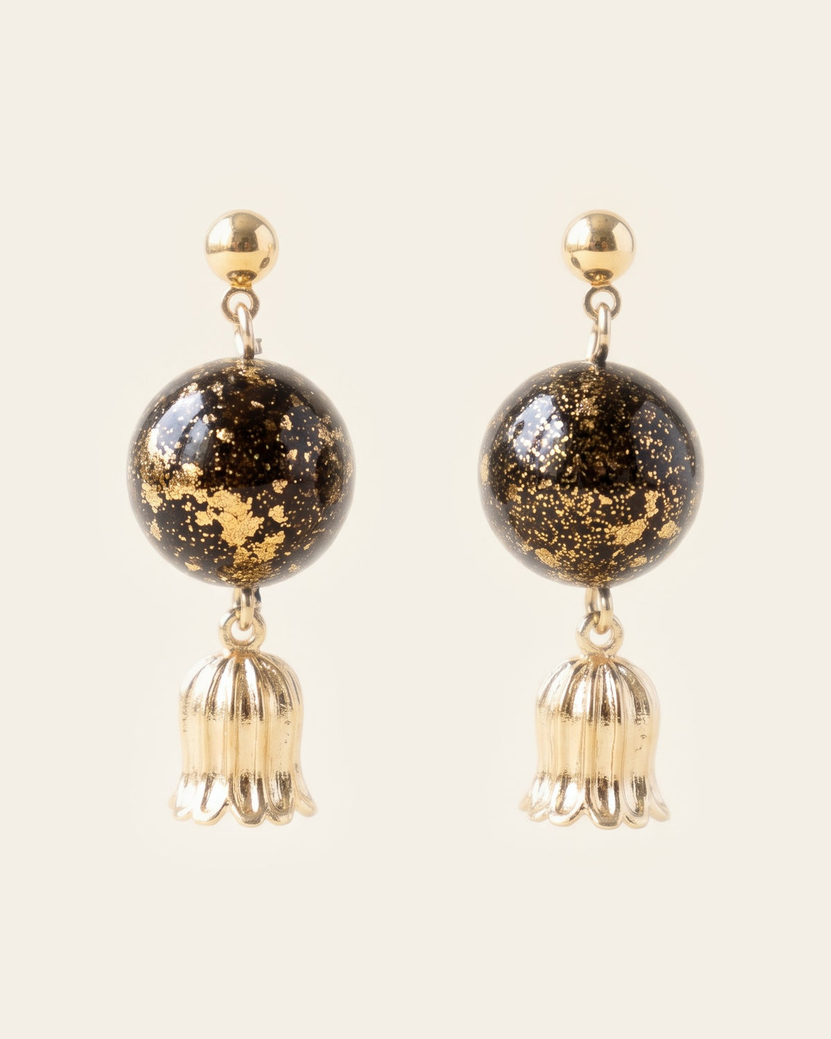 Pair of drop earrings with gold ball studs, dark lacquer spheres flecked with gold leaf and fluted gold bellflower charms, on an ivory background