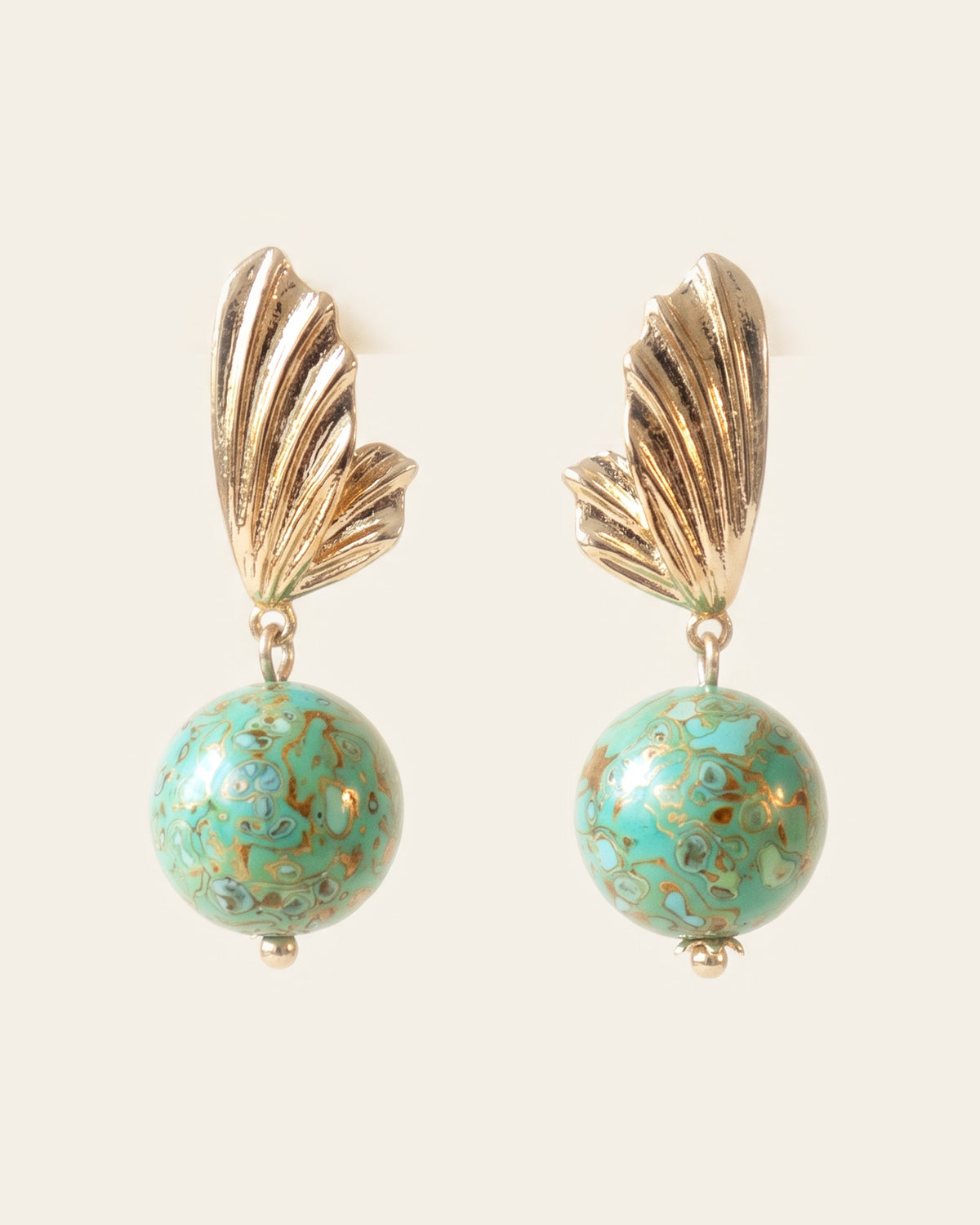 Pair of turquoise-green xipi lacquer sphere earrings with gold marbling and mother-of-pearl flecks, hanging from ribbed gold wing-shaped studs, on an ivory background